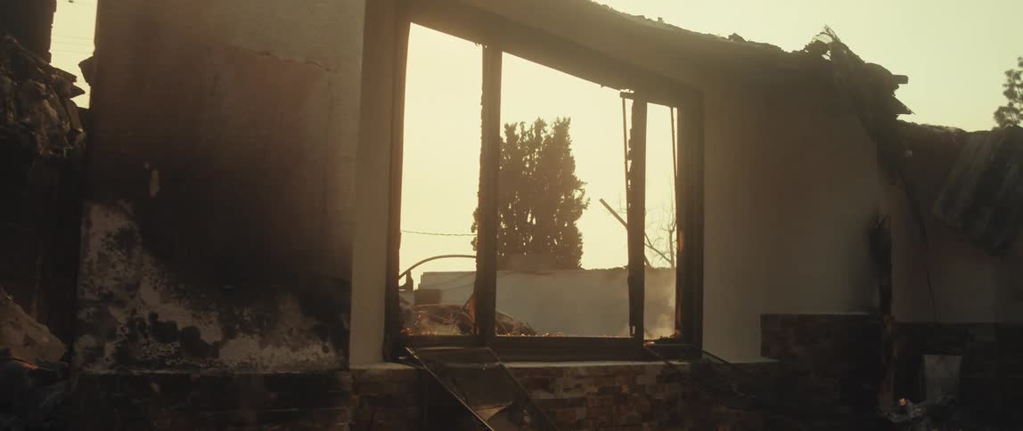 A tree is visible through the empty window frame of a dilapidated building against a hazy sky