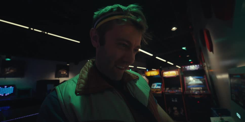 A man with a headband is playing a game and is happy and moving his head and the lights on the screen illuminate the man