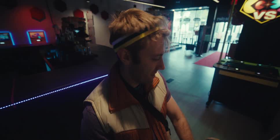 A man with a headband is playing an arcade game and is shaking his head