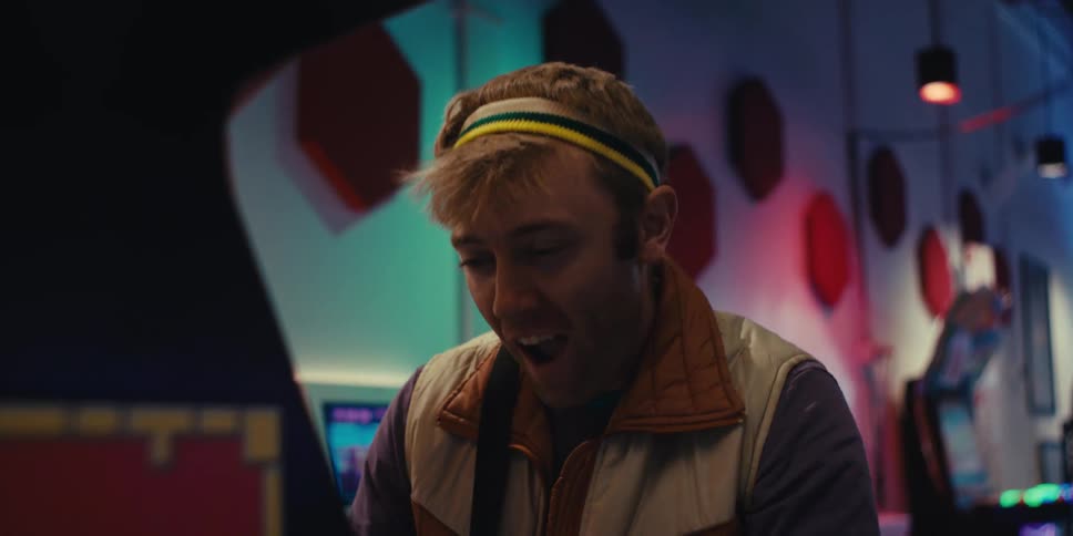 A close up of a young man wearing a colorful headband enjoying playing video games on an arcade machine