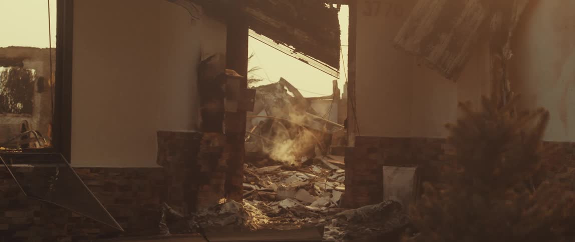 The interior of a dilapidated building is visible through a doorway revealing rubble and destruction within under a hazy sky