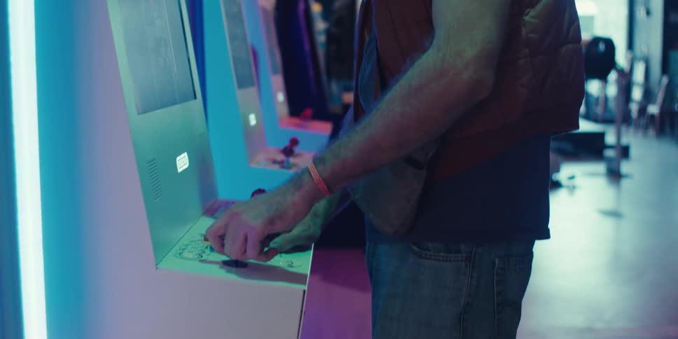 A closeup of a young man wearing a colorful bandana enjoying playing video games on an arcade machine