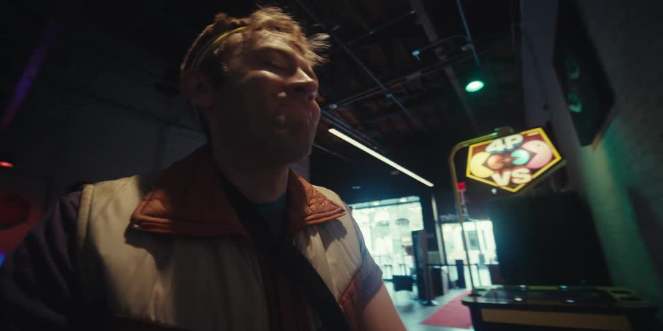 The face of a young man who is playing at an arcade and he has a headband on his head and gives a subtle smile