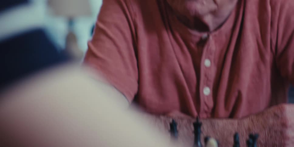 Elderly man sitting and talking to another person while playing chess