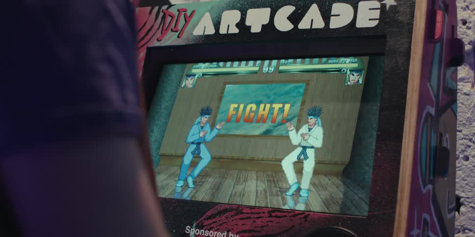 A person looks at a retro arcade game on a screen showing two characters facing off in a match