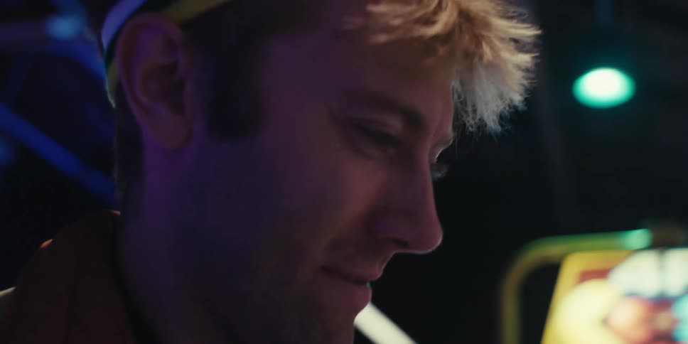 A close up of a young man wearing a colorful headband enjoying playing video games on an arcade machine