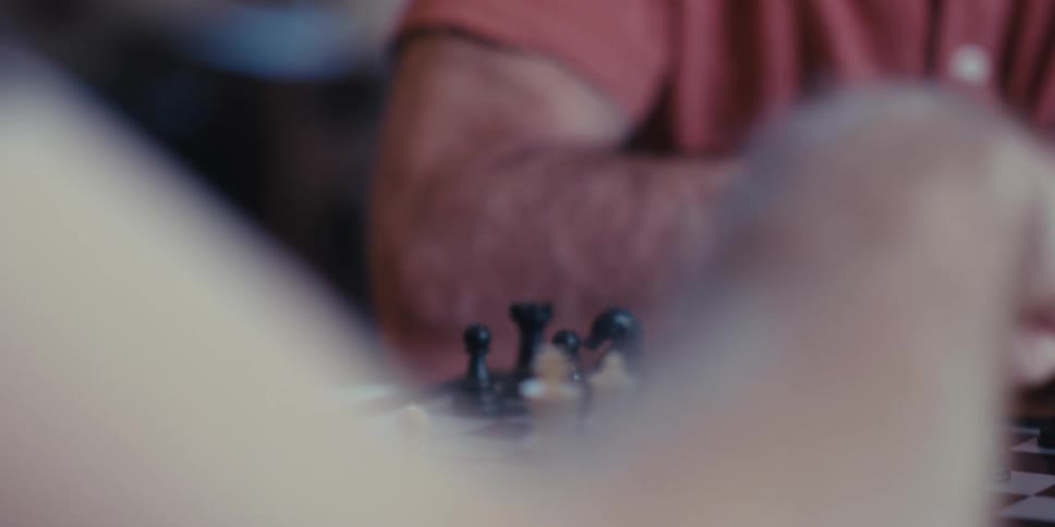 An elderly man playing a game of chess with another person