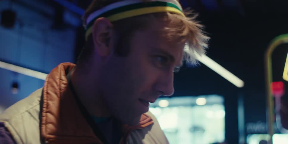 A closeup of a young man wearing a colorful bandana enjoying playing video games on an arcade machine