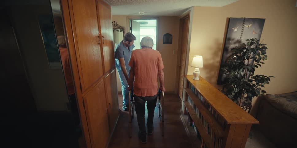 Elderly patient walking with a walker and next to a nurse