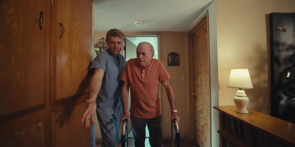 Elderly man walking down a hallway accompanied by a nurse