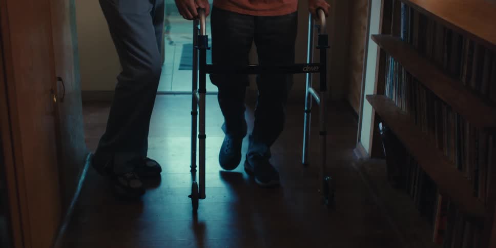 A male nurse assists an elderly patient with walking using a walker at home