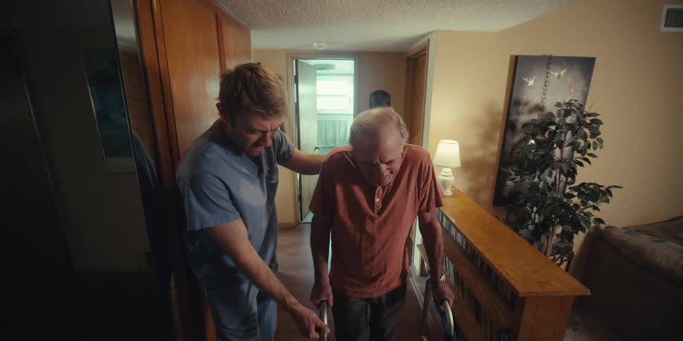 Elderly patient walking alongside a nurse with the help of a walker down a hallway