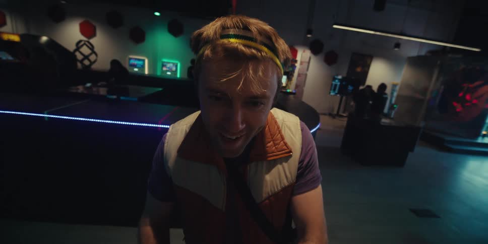 A close up of a young man wearing a colorful headband enjoying playing video games on an arcade machine