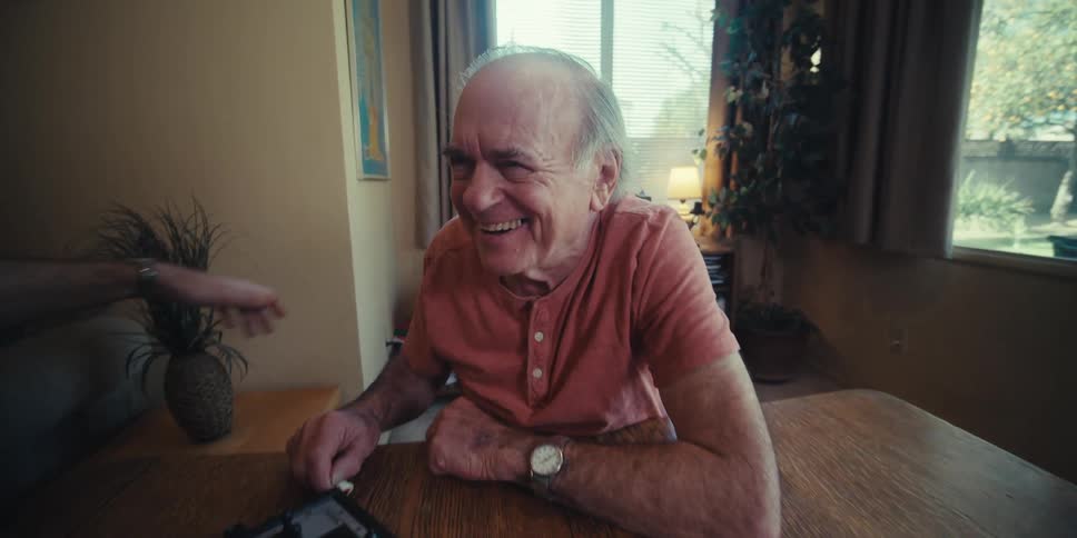 A young man praises an elderly man for a clever move during their chess game at home
