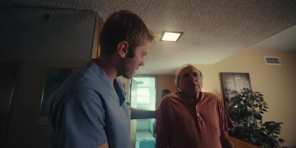 Nurse assisting an elderly man to walk indoors in a hallway