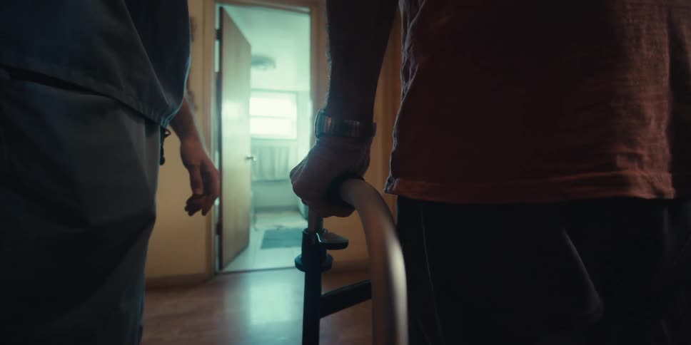 A home health aid helps an older man use a mobility walker in his home