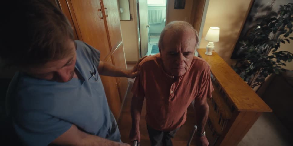 Nurse helping an elderly man walk with the aid of a walker