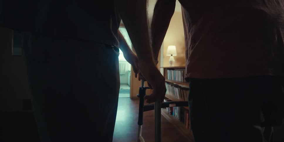 A nurse assists a man with a walker down the hall
