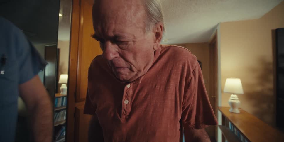 A male nurse encouraging an elderly man using a walker to walk down the corridor of his home
