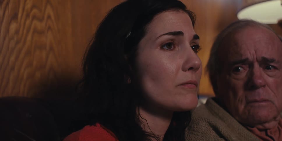 Elderly man glances toward a younger woman as they sit together looking sad