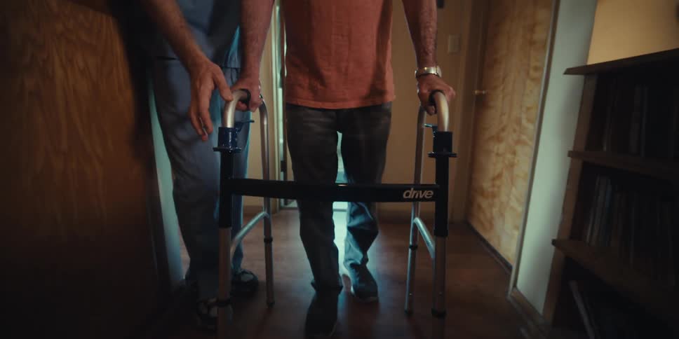 Elderly man walking with a walker with the help of a nurse