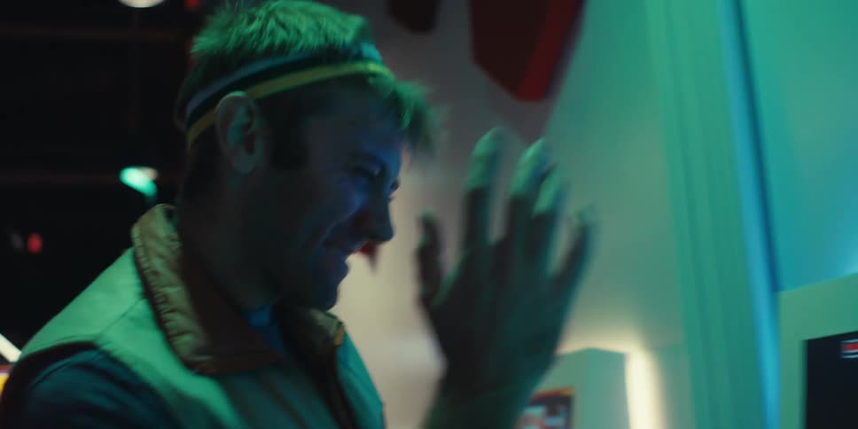 The face of a young man with a headband and he is playing a game on a screen that is shining on his face