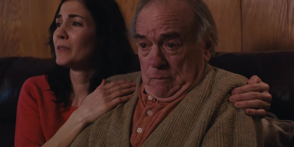 An elderly man and a young woman possibly family sitting together on a couch at home crying and in disbelief after receiving bad news