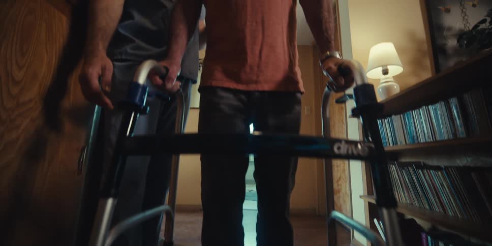 A nurse is helping a man with a walker down the hall