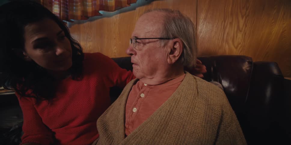 Daughter sitting next to elderly father on a sofa running her hands over his back