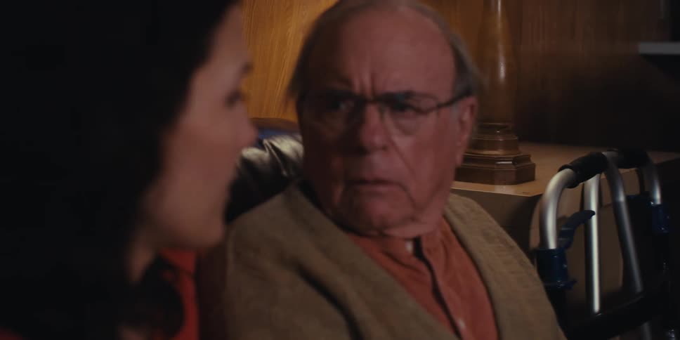 A man points to a paper in the hand of an elderly man and he begins to talk to a woman who is next to him