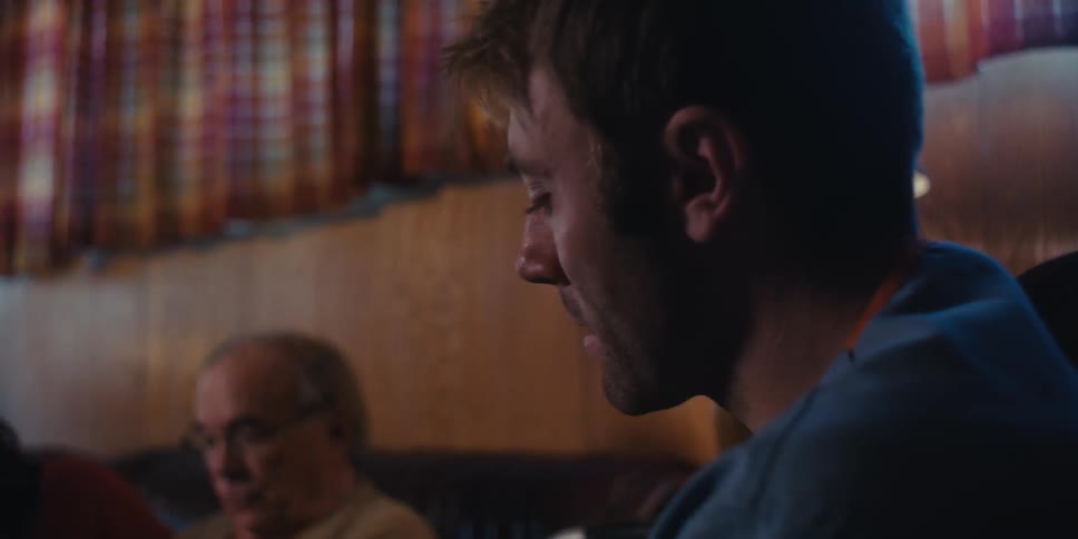 A young man talking with a smile to an elderly man who is sitting on the sofa next to a woman