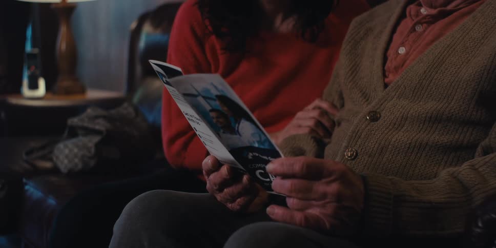 Elderly man and woman sitting on sofa looking at medical brochure