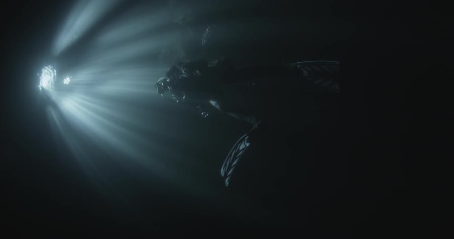 A diver swims up in the dark water