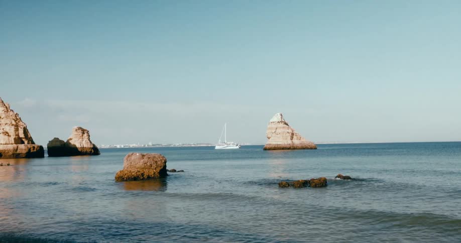 Landscape of a beach with rocks in the middle of the sea and a boat in the background