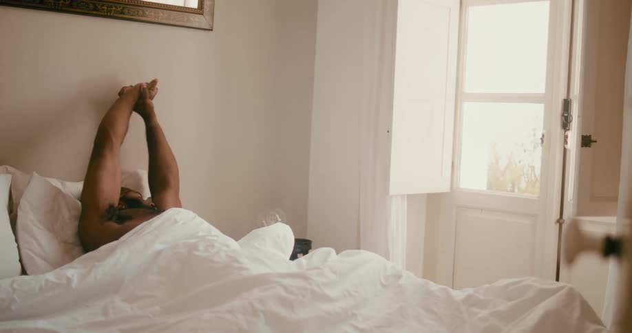 Bearded man with a headband gets up from bed in the bedroom