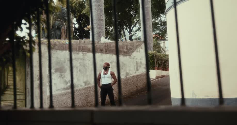 Man in white tank top next to a wall of an urban house on the street