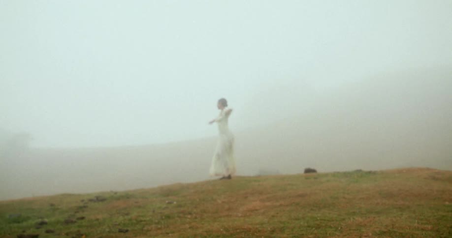Woman in a white dress spinning on a foggy hill