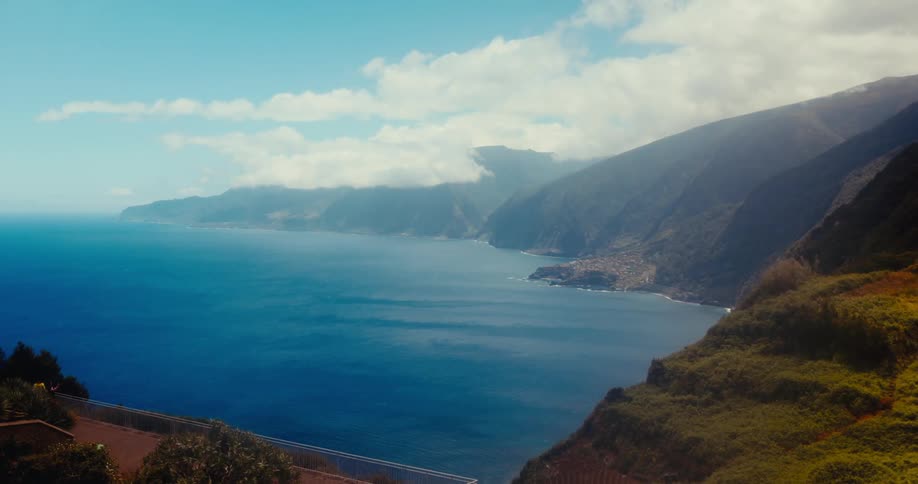Green mountains meet the vast blue ocean under a partly cloudy sky