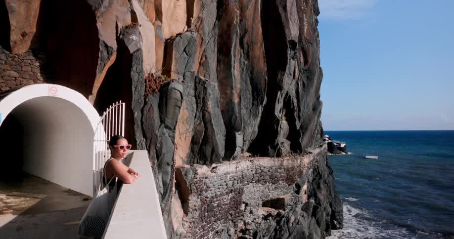 Woman in sunglasses enjoying the view from a high hill with a rocky wall by the sea