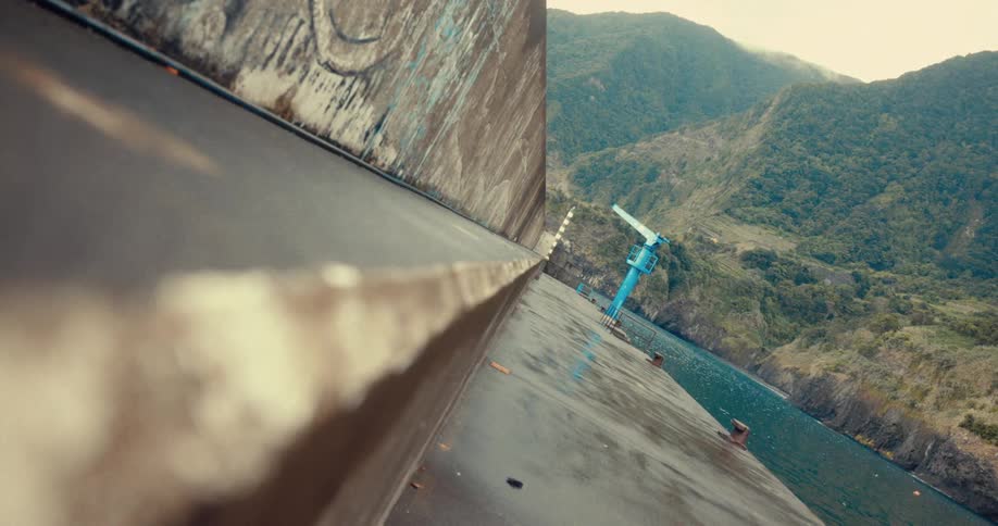 A concrete dam wall stretches into a distant valley with a sliver of water visible below