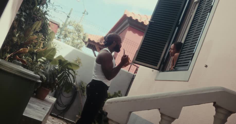 Woman at the window of a house handing a mug to a man who is smoking a pipe and they talk