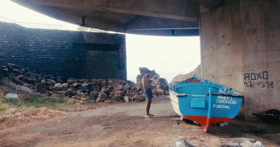 A clip of a man walking under a bridge beside a blue boat