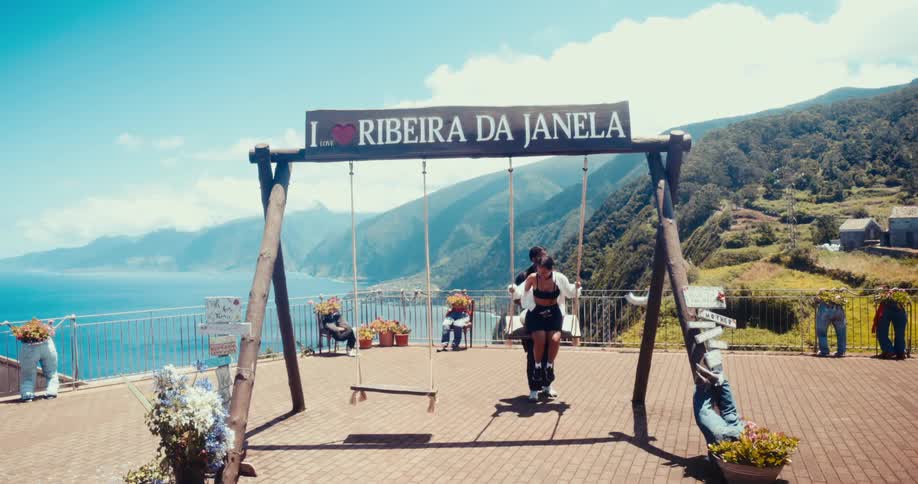 Man pushing a woman on a swing at a viewpoint with the sea in the background