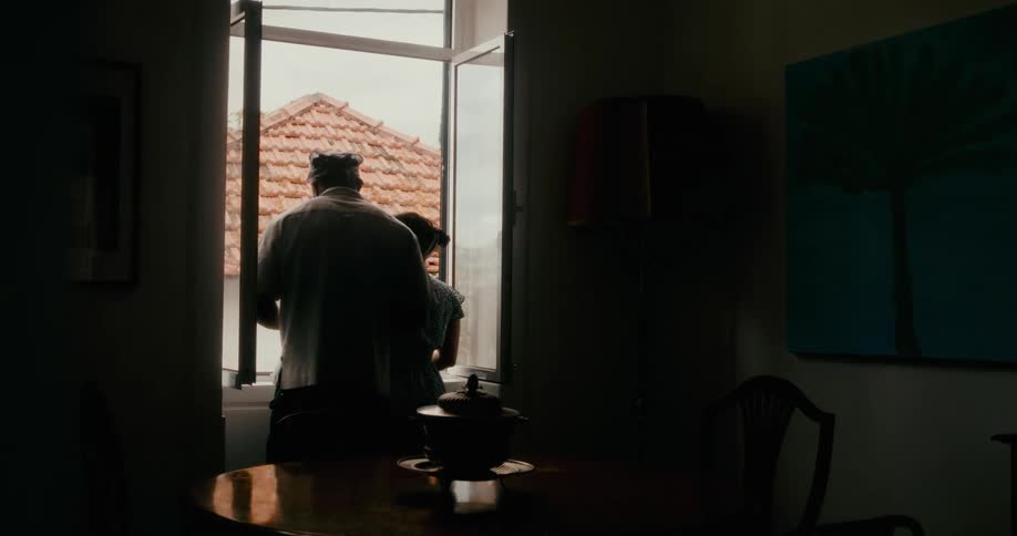 Man approaching a woman who is standing at the window of a house