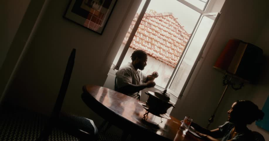 Man sitting next to a window smoking a pipe and a woman next to him