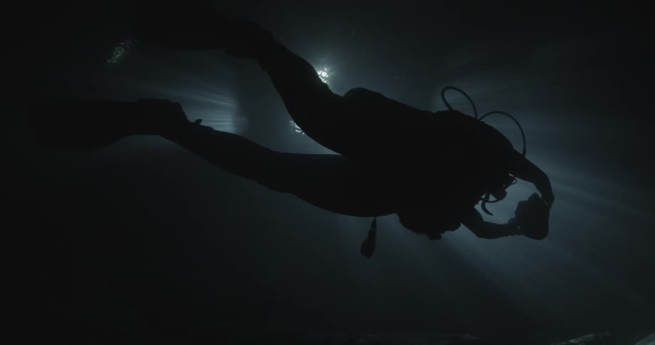 A scuba diver swims in the dark water