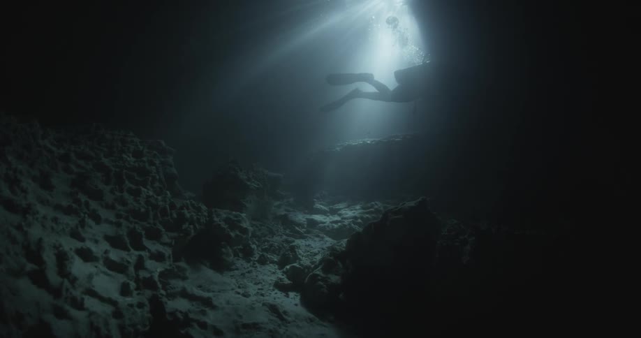 Scuba diver silhouette seen swimming through rays of light in a shallow area