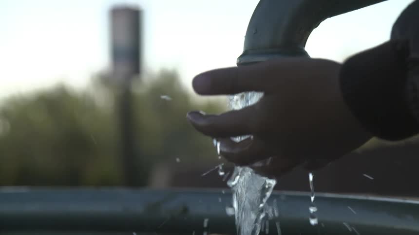 Water pouring from a faucet over a persons hand outside