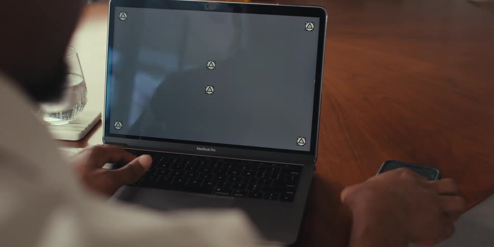A person is holding a smartphone in one hand and using a macbook pro laptop with the other both devices displaying a screen with a grey replaceable screen