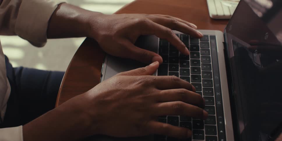 Man wearing a brown shirt types on a laptop
